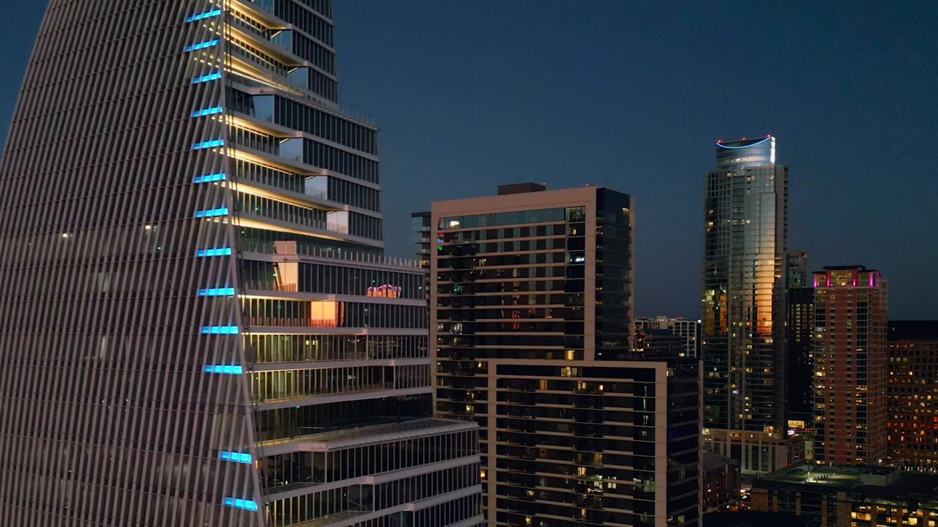 Glass skyscraper with lit edges beside other towers at dusk